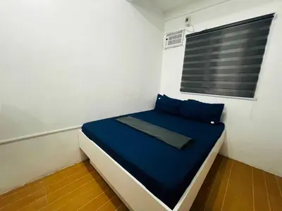 a small room with a bed with blue sheets and a window at T&A Building in Manila
