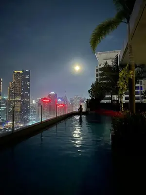 a person standing on the edge of a swimming pool at night at Tahanan Studio at Salcedo Skysuites in Manila