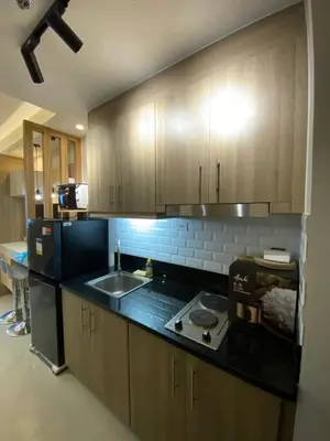 a kitchen with wooden cabinets and a black counter top at Luxe Studio at Fame Residences Malls, CBDs and More in Manila