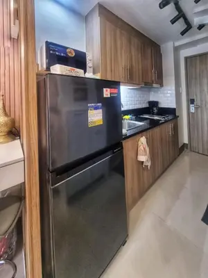 a kitchen with a stainless steel refrigerator and wooden cabinets at Luxe Studio at Fame Residences Malls, CBDs and More in Manila