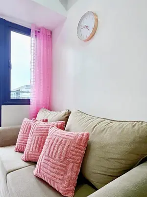 a couch with pink pillows and a clock on a wall at Cozy Modern Condotel in Pasay Near MOA & Airport in Manila