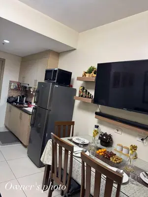 a kitchen with a table and a refrigerator and a television at Juvrey Studio-Unit Breeze Residences in Manila