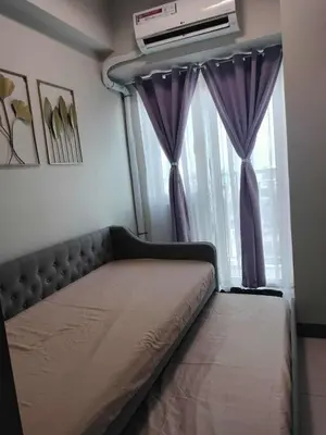 a bed in a room with purple curtains and a window at Gavinne Place Coast Residences in Manila