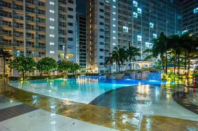 a large swimming pool with palm trees and buildings at Relaxing Hotel Apartment Stay : Near MOA & Airport in Manila
