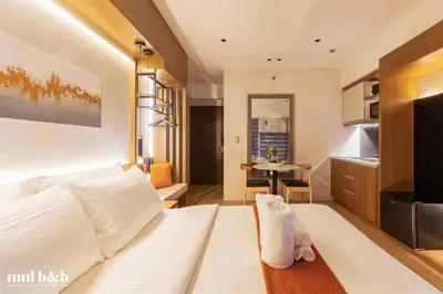 a bedroom with a white bed and a kitchen at Near Venice Mall! Hotel 1BR Unit in Viceroy Residences in Manila