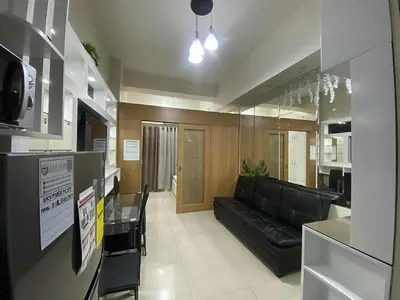 a living room with a black couch and a kitchen at Shell Residences Mall of asia Pham in Manila