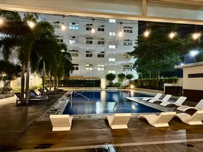 a swimming pool with white chairs and a building at J&A Cozy Calm Stay in Biñan