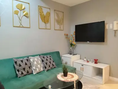 a living room with a green couch and a flat screen tv at Beach Bliss Your 2 BR Condo Retreat Awaits in Manila