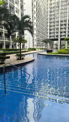 a large swimming pool with palm trees and buildings at Urban Haven Manila in Manila
