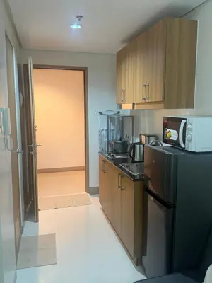 a kitchen with a black refrigerator and wooden cabinets at The Vibe at SMDC The Lush Residences in Manila