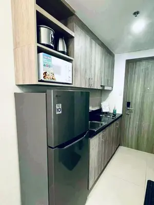 a kitchen with a black refrigerator and wooden cabinets at JL's City Hideaway at Fame Residences in Manila