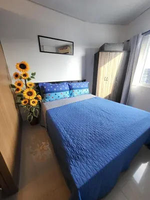 a bedroom with a blue bed and a vase with sunflowers at Shell Residences Condo in Manila