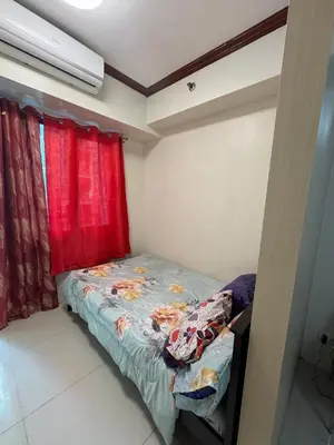 a small bed in a room with red curtains at Melas Condotel in Manila