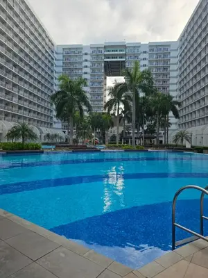 a large swimming pool in front of two large buildings at Cozy 1BR Balcony Pool View with WiFi & Netflix near MOA and NAIA Airport in Manila