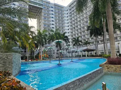 a large swimming pool with palm trees and buildings at Cozy 1BR Balcony Pool View with WiFi & Netflix near MOA and NAIA Airport in Manila