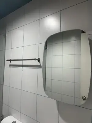 a white tiled bathroom with a toilet and a mirror at Bleau Haven KL Service Residences Makati in Manila