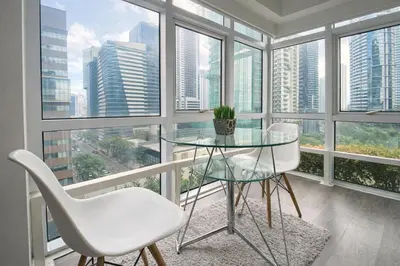 a glass table and two white chairs in a room with windows at Stylish Stay in BGC 5th Ave with Free Parking in Manila