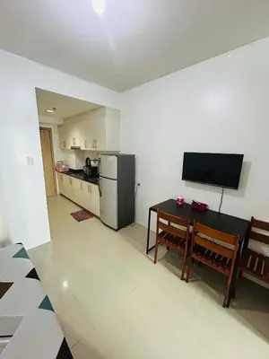 a kitchen with a refrigerator and a table and a television at Sea Residences MOA-Eric Apartments in Manila