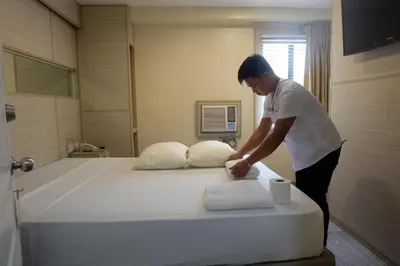 a man standing next to a bed with pillows at Spaces Hotel Makati in Manila
