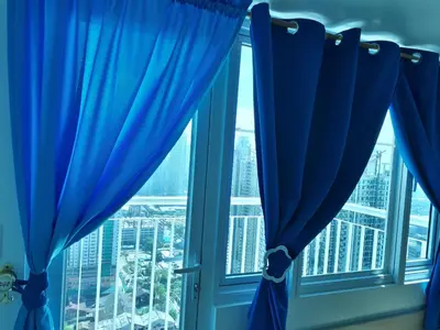 a window with blue curtains looking out at the city at Light Residences 1BR Apartment Balcony in Manila