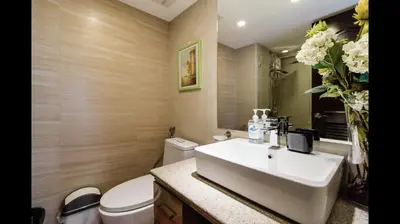 a bathroom with a sink and a toilet and a vase of flowers at Grand Apartment near BGC in Manila