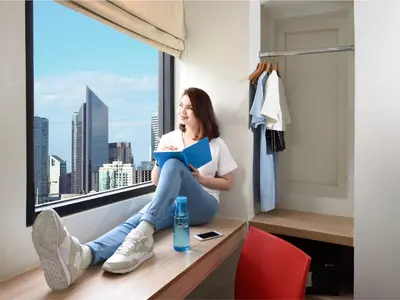 a woman sitting on a window sill reading a book at Hop Inn Hotel Alabang Manila in Manila