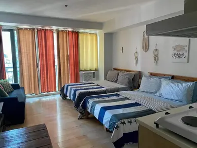 a room with two beds and a couch and windows at GREENFIELD studio w/ 2 queen across Shangrila in Manila