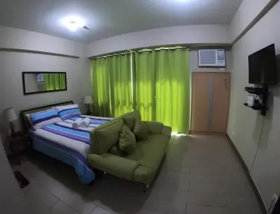 a bedroom with a bed with a green curtain and a couch at Palm Tree 2 Villas-Cluster 2 Unit 3N in Manila
