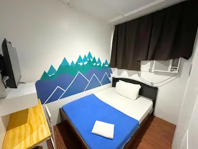 a small bedroom with a blue bed with a mountain mural at Dormitelsph UST in Manila