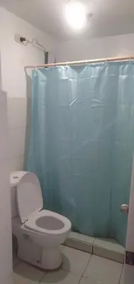 a bathroom with a toilet and a blue shower curtain at EKONUMI ROOMS at Moonwalk Paranaque in Manila
