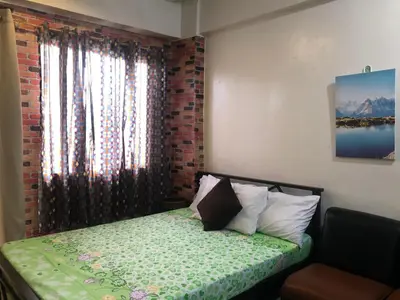 a bedroom with a bed and a window with a green blanket at Your City•Home Apartment in Manila