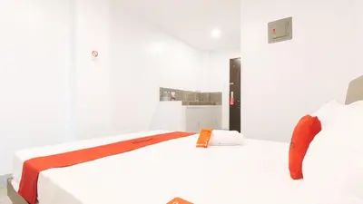 a white bedroom with a white bed with orange accents at RedDoorz near Zobel Roxas St in Manila