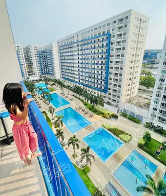 a little girl standing on a balcony looking out at a resort at Sea Residences by JH & LD's Condotel in Manila