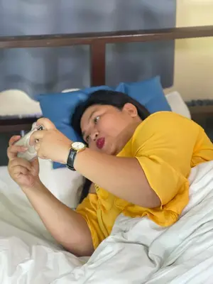 a woman laying in a bed drinking from a bottle at airobedz MANILA - A Value Hotel in Manila