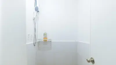 a shower in a white tiled bathroom at Eimys Place at Urban Deca Mandaluyong by RedDoorz in Manila