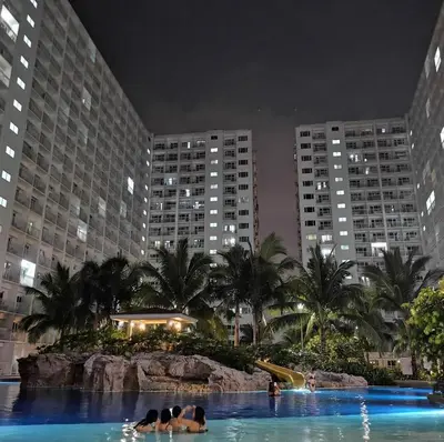 a hotel swimming pool with people in the water at night at SHORE RESIDENCE d6, shortwalk Mall of Asia near Airport in Manila