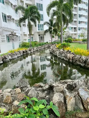 a pond in front of a building with palm trees at At Home Condo With Free Pool Access in Manila