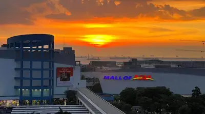 a sunset over a building with a mall of signs on it at Madison's Place at Sea MOA in Manila