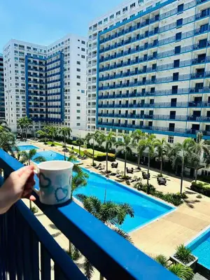a person holding a coffee cup on a balcony overlooking a pool at Sea Residences - Val Alano in Manila