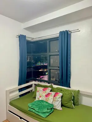 a bed in a room with a window with blue curtains at 2BR w Balcony in Araneta, Cubao w Pool and Gym - Porto Vita in Manila