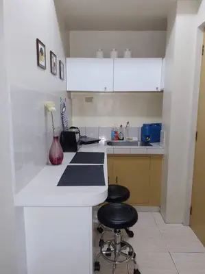 a white kitchen with two stools at a counter at Affordable Transient along Ortigas Ext in Cainta