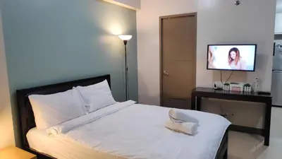 a bedroom with a white bed with a flat screen tv at Palm Tree Villas Condominium by Beth in Manila