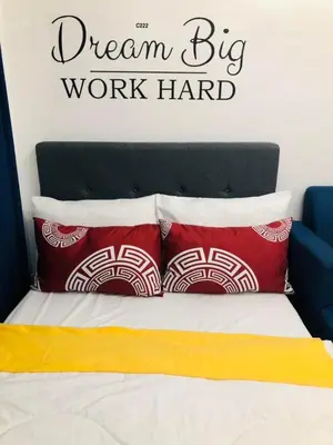 a bed with two red pillows and a dream big work hard sign above it at Avida Tower Sucat, comfortable studio type in Manila
