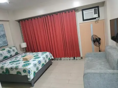 a bedroom with a bed and a couch and a red curtain at RQUI CONDOTEL NEWPORT PASAY in Manila
