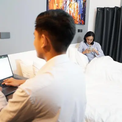 a woman sitting on a bed looking at her cell phone at mySTAY Hotel BGC West in Manila