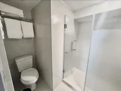 a white bathroom with a toilet and a shower at Stylish loft, 65 in UHDTV w Fast WiFi + Pool & Gym in Manila