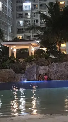 two people sitting next to a swimming pool at night at EZStays Shore Residences in Manila