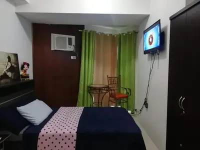 a bedroom with a bed and a tv and green curtains at Grand riviera suites Studio Type Only in Manila
