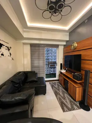 a living room with a black leather couch and a flat screen tv at Lumiere suites in Manila