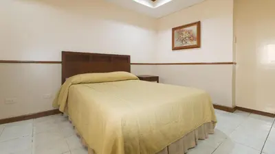 a bedroom with a bed with a yellow blanket on it at Garden Plaza Hotel Manila in Manila